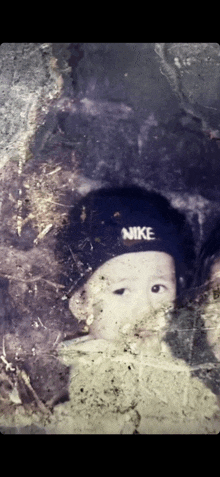 a baby wearing a black nike hat is looking at the camera