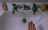 a person 's hand is reaching into a bathroom sink with a red knob on the faucet