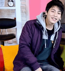 a young man wearing a purple jacket is sitting on a couch and smiling