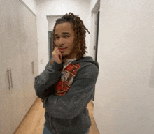 a young man with dreadlocks is standing in a hallway with his arms crossed and his hand on his chin