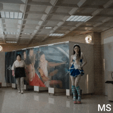 a woman in a blue dress is standing in front of a wall with pictures of women on it