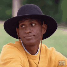a man wearing a black hat and a yellow shirt with the great american baking show written on the back