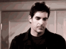 a man in a black jacket and black shirt is standing in front of a door and looking down .