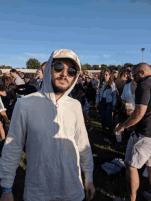 a man wearing sunglasses and a hoodie stands in a crowd