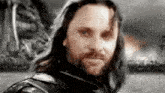 a man with long hair and a beard is wearing a leather jacket and looking at the camera .