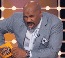 a man wearing a suit and tie is holding a trivia feud sign