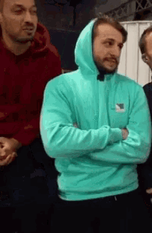 a man in a blue hoodie stands with his arms crossed