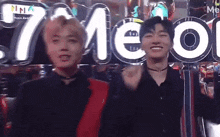 a couple of young men are standing next to each other in front of a sign that says ' meo ' on it .