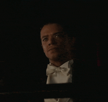 a man in a tuxedo and bow tie looks out a window in the dark