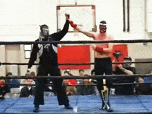 a wrestler wearing a mask is giving a high five to another wrestler in a boxing ring