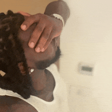 a man in a white tank top holds his hand to his head
