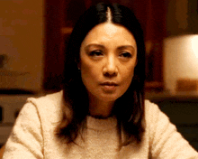 a woman in a white sweater looks at the camera with a serious look on her face