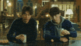 two men sitting at a table with a can of beer and an egg