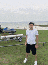 a man in a white shirt and black shorts stands in front of a jet ski on a trailer