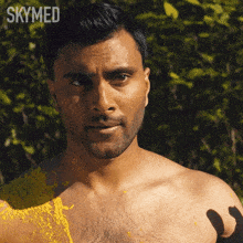 a shirtless man is covered in yellow paint and the word skymed is on the bottom right