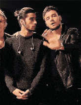 a man wearing a black sweater and a leather jacket stands next to another man