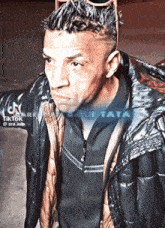 a man wearing sunglasses and a black jacket has a tiktok watermark on his jacket