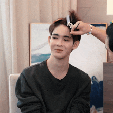 a man in a black shirt is getting his hair styled