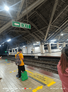 a green exit sign hangs above a train station platform