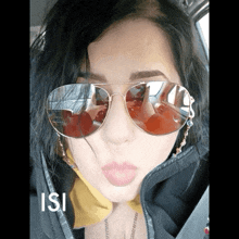 a woman wearing sunglasses and a yellow scarf has the letters isi below her face