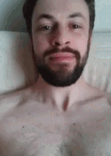 a shirtless man with a beard is laying in bed