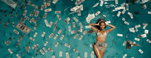 a woman in a bikini is laying in a pool surrounded by money