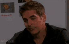 a man in a black shirt is sitting in front of a white board with evidence on it .