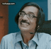 a man wearing glasses and a headset is smiling while talking on a phone .