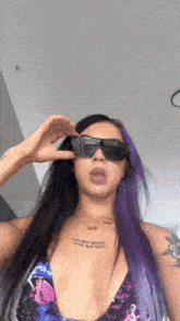 a woman with purple hair is wearing sunglasses and a tattoo on her chest