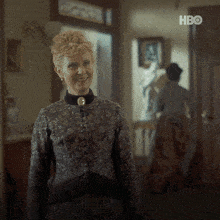 a woman is smiling in a hallway with a hbo logo in the background