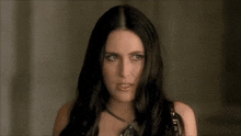 a woman with long black hair is wearing a necklace and looking at the camera