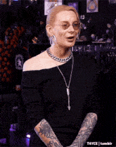 a woman with tattoos on her arms is wearing a black dress and a chain necklace .