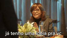 a woman with glasses sits at a table with the words " ja tenho uma ideia pra vc " above her