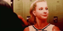 a cheerleader is smiling in a locker room while a man looks on .