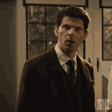 a man in a suit and tie is standing in front of a window looking at the camera .