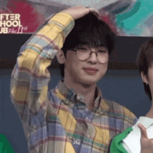 a young man wearing glasses and a plaid shirt has his hand on his head