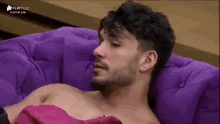 a shirtless man is laying on a purple couch with a pink towel around his neck .