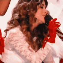 a woman singing into a microphone with red gloves
