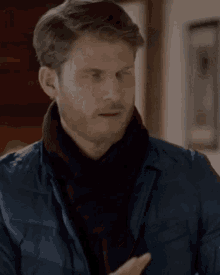a man wearing a scarf and a jacket is making a gesture with his hands .