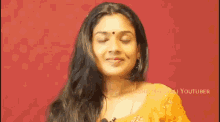 a woman in a yellow saree is smiling and waving her hand .