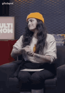 a woman wearing a yellow beanie sits in a chair in front of a sign that says " ulti show "