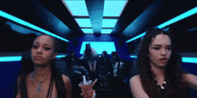 a woman holding a cup with a straw is standing next to another woman in a dark room