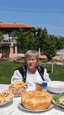 an elderly woman sits at a table with plates of food and a bottle of spice