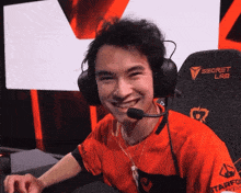 a man wearing headphones and a secret lab shirt smiles