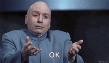 a bald man in a blue suit says ok with his hands