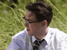 a man wearing glasses and a tie is sitting in a field of tall grass