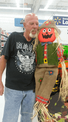 a man wearing a navy shirt is posing with a scarecrow