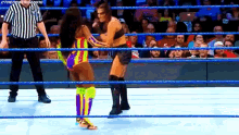 two women are wrestling in a wrestling ring with a referee standing behind them .