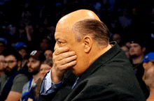 a bald man covering his face with his hand in a crowd