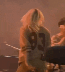 a woman in a number 93 shirt is standing on a stage holding a microphone in her hand .
